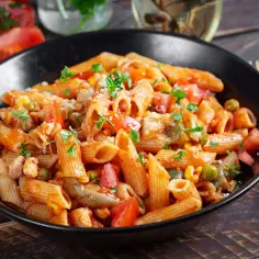 Makaron penne z pieczarkami, pomidorami i zielonym groszkiem w sosie, posypany parmezanem i ziołami.